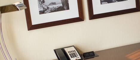 Una habitación de hotel con un escritorio de madera, un teléfono y fotografías enmarcadas en la pared.