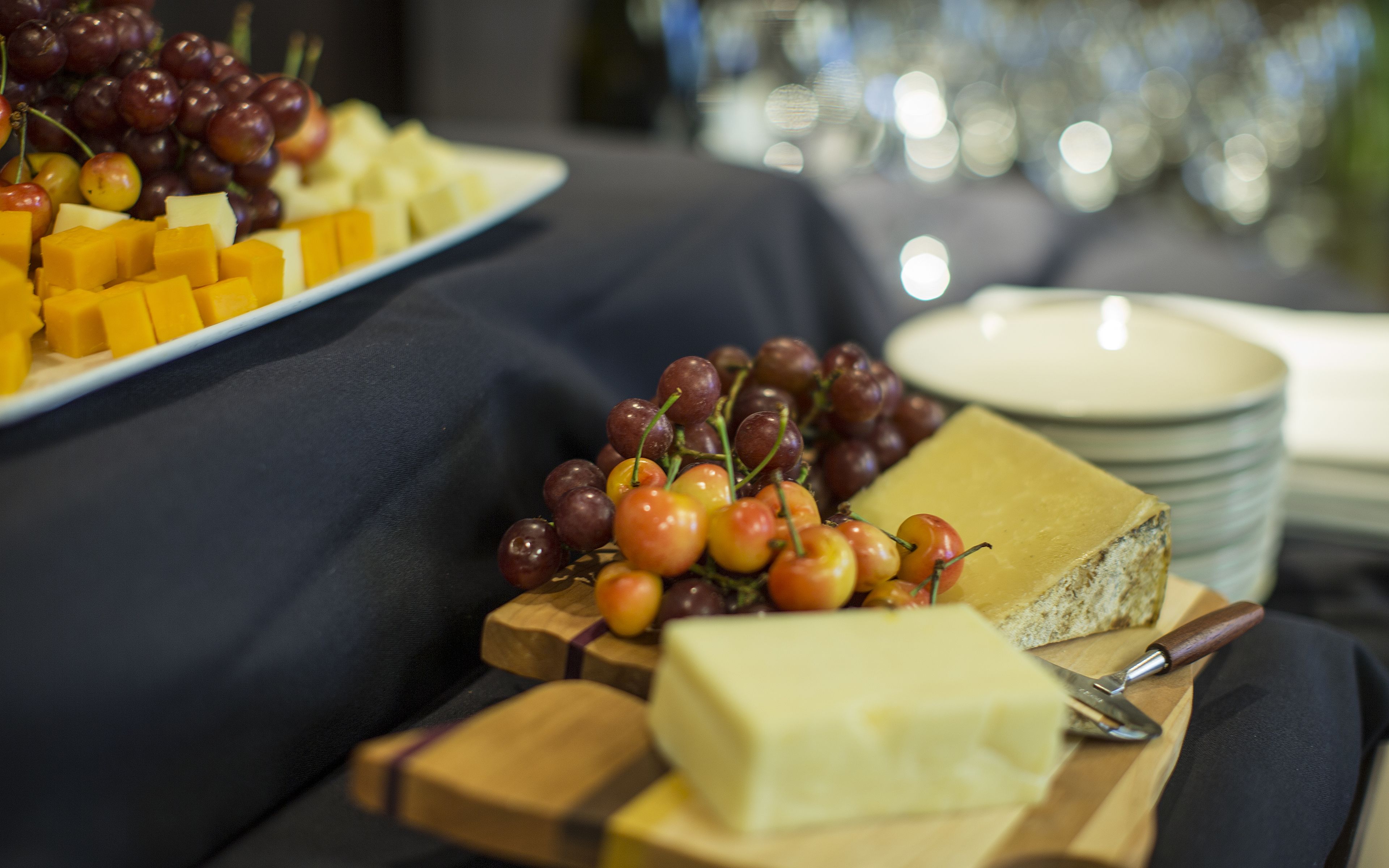 A cheese board with various cheeses and grapes on a wooden cutting board.