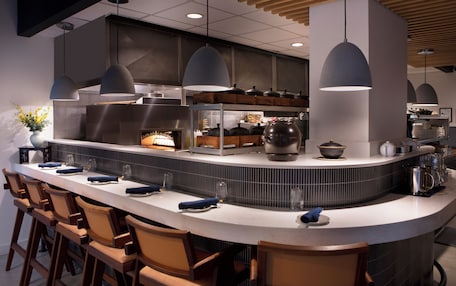 A modern kitchen with a curved island, bar stools, pendant lighting, and a variety of kitchen appliances.