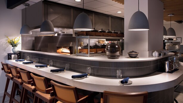 A modern kitchen with a curved island, bar stools, pendant lighting, and a variety of kitchen appliances.