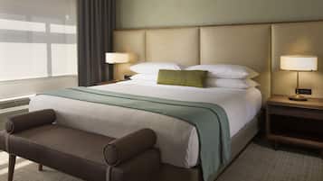 A hotel room with a large bed, a bedside table with a lamp, a chair, and a window with curtains.