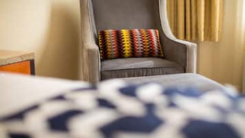 Una silla con un cojín estampado, una cama con una colcha azul y blanca estampada, y una cortina al fondo.