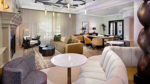 A modern hotel lobby with a fireplace, comfortable seating, a dining area, and a chandelier.