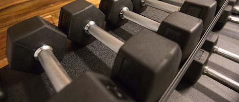 A row of black dumbbells on a rack with a wooden floor.
