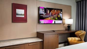 Habitación de hotel con cama, escritorio, silla, televisor montado en la pared y un cuadro enmarcado.