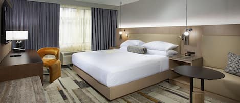 Habitación de hotel con cama, mesitas de noche, un escritorio con lámpara, una silla y una pequeña mesa redonda.