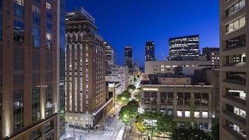A cityscape at dusk with modern buildings, a prominent Roosevelt Hotel, and a street lined with trees.