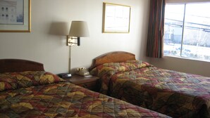 A hotel room with two beds, a bedside table with a lamp, a telephone, and framed pictures on the walls. - Seattle Pacific Hotel (Seattle)