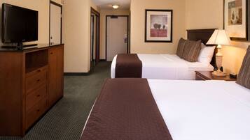 A hotel room with two beds, a TV, a desk, and a lamp.