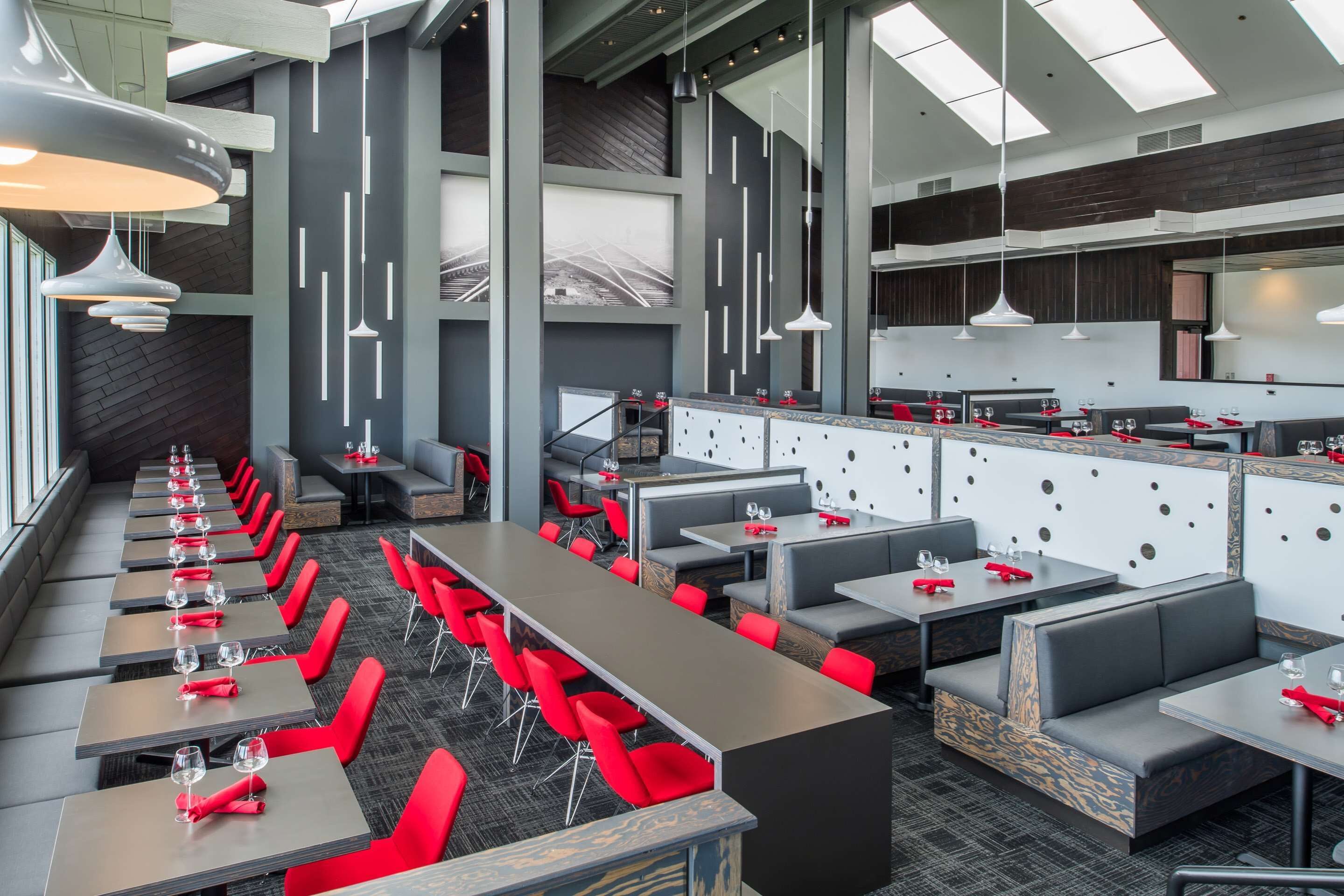Un restaurante moderno con largas mesas comunitarias y sillas rojas, techos altos e iluminación colgante.