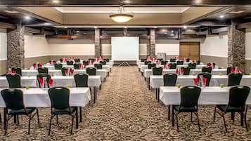 A conference room with rows of tables and chairs, a projector screen, and a carpeted floor.