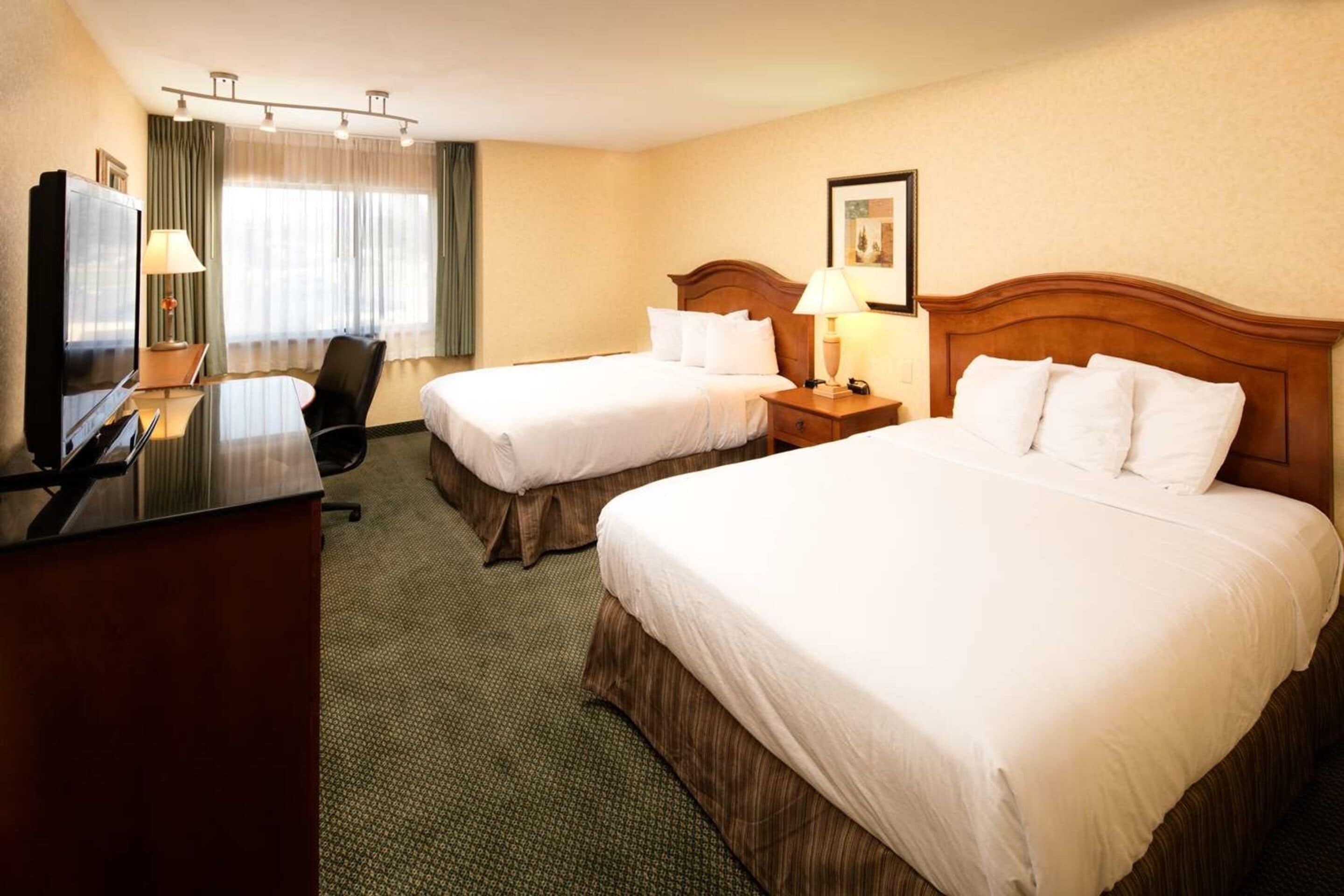 A hotel room with two beds, a desk with a TV, and a chair.