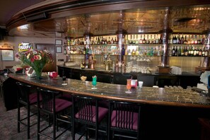 A bar area with a marble countertop, multiple bar stools, and a variety of bottles and glasses on shelves. - Red Lion Hotel Yakima Center (Yakima)