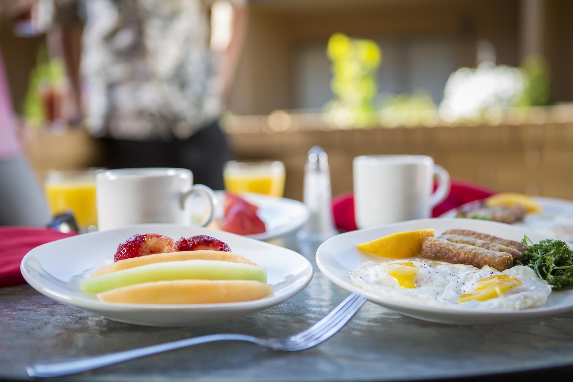 Una escena de desayuno con platos de comida, incluyendo frutas y huevos, sobre una mesa.