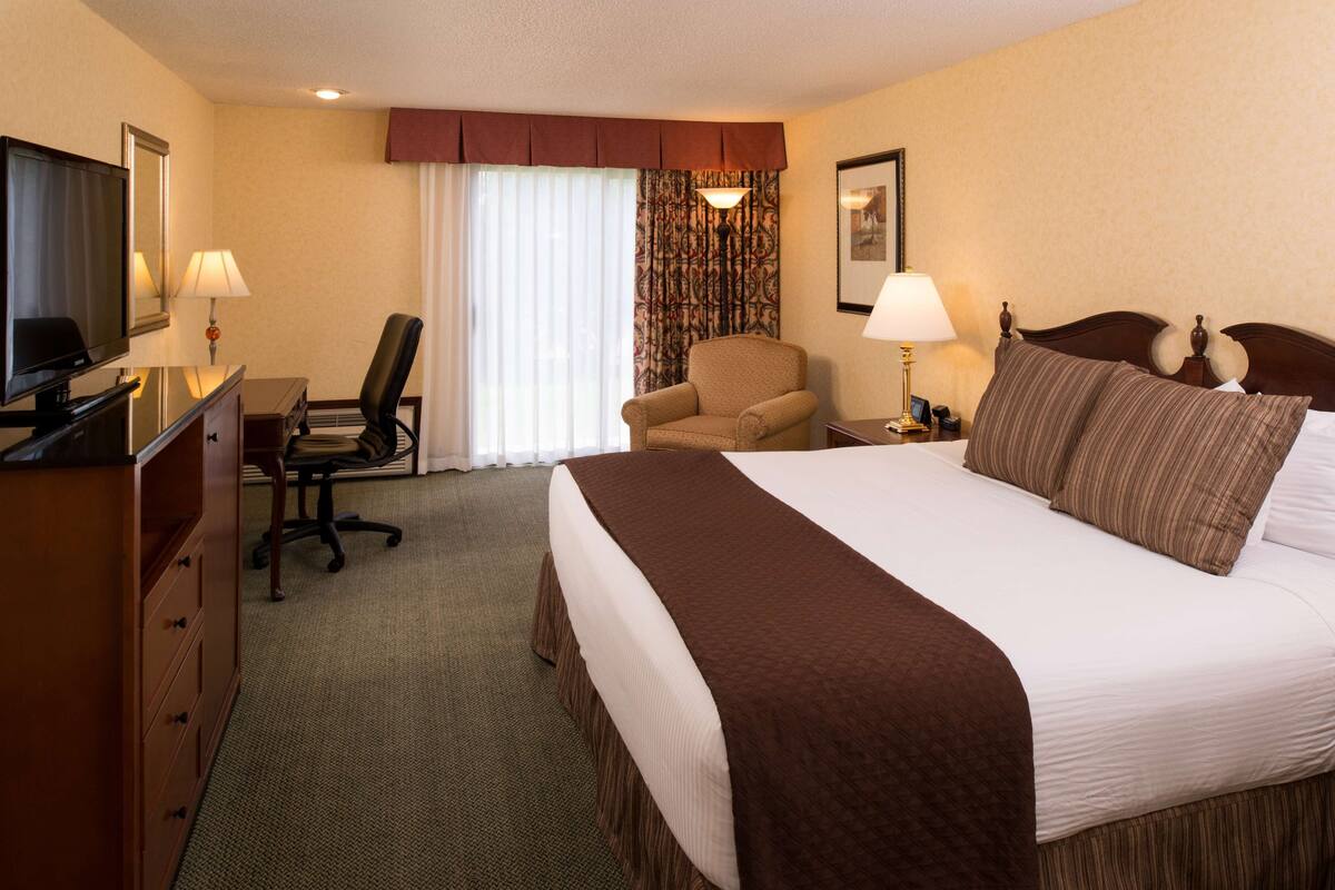 A hotel room with a large bed, a desk with a chair, a television, and a lamp.
