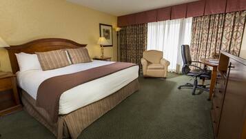 A hotel room with a large bed, a desk, a chair, and a dresser.