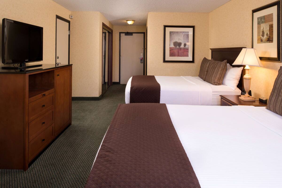 A hotel room with two beds, a television, a desk, and a lamp.
