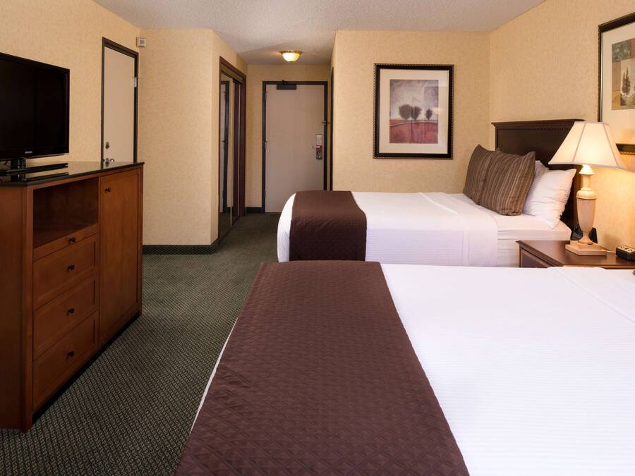 Quarto de hotel com duas camas, televisão, escrivaninha e abajur.