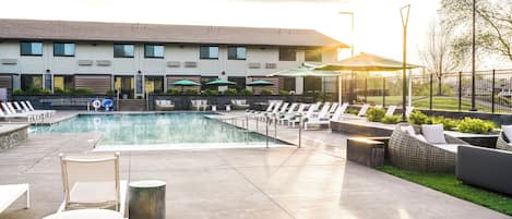 A modern hotel with a swimming pool, outdoor seating, and a well-maintained garden.