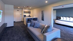 A modern hotel room with a grey sofa, a small coffee table, a bed with white bedding, a kitchenette, and a view of the cityscape. - Ruby River Hotel Downtown Spokane (Spokane)