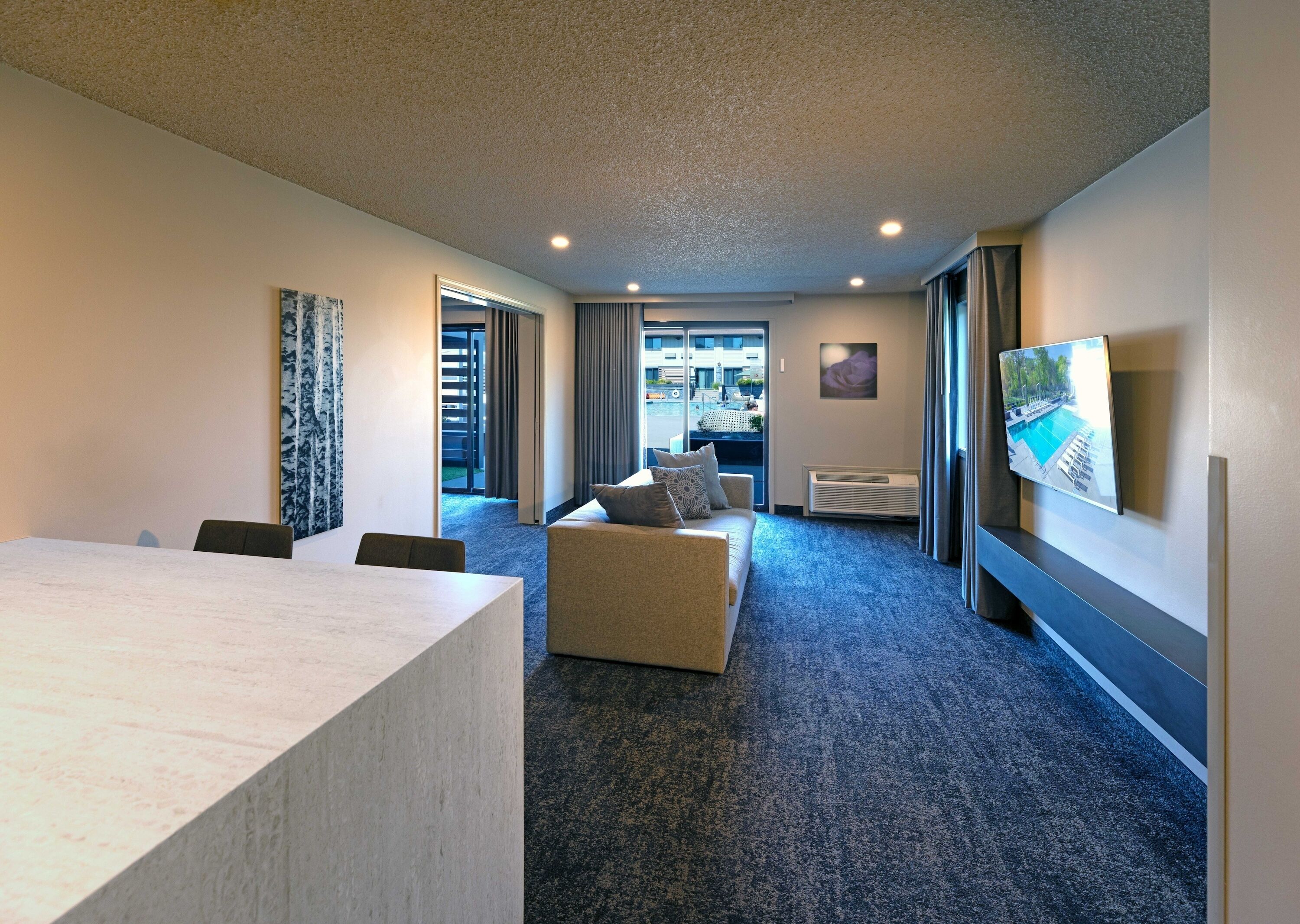 A hotel room with a large bed, a desk, a chair, a sofa, a TV, and a view of the outside.