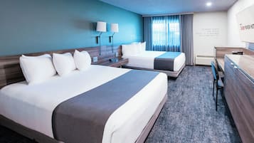 Ein Hotelzimmer mit zwei Betten, einem Schreibtisch, einem Stuhl, einer Lampe und einem Fenster mit Vorhängen.