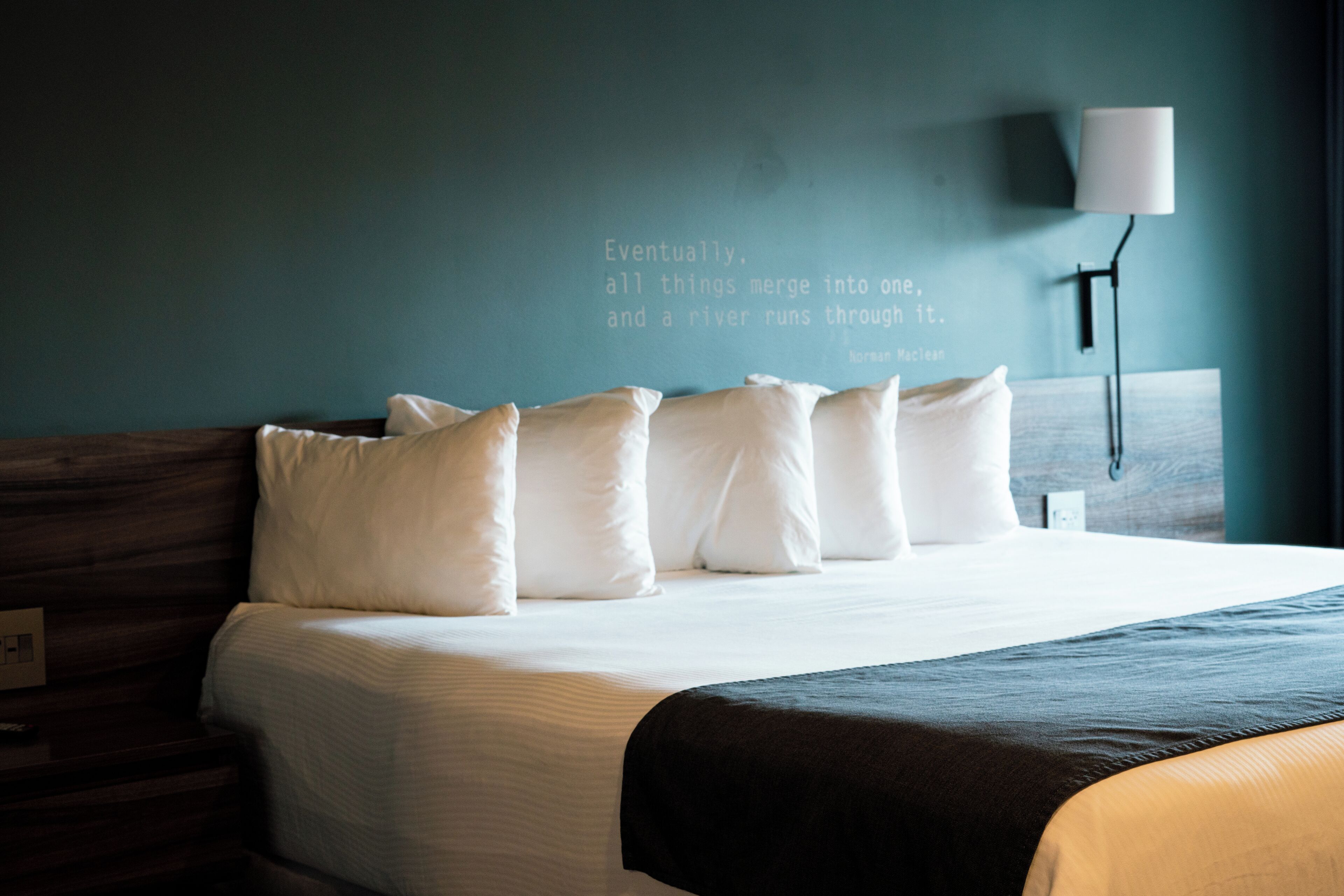 A neatly made bed with white bedding and a dark throw blanket. A wall-mounted lamp is visible to the right.