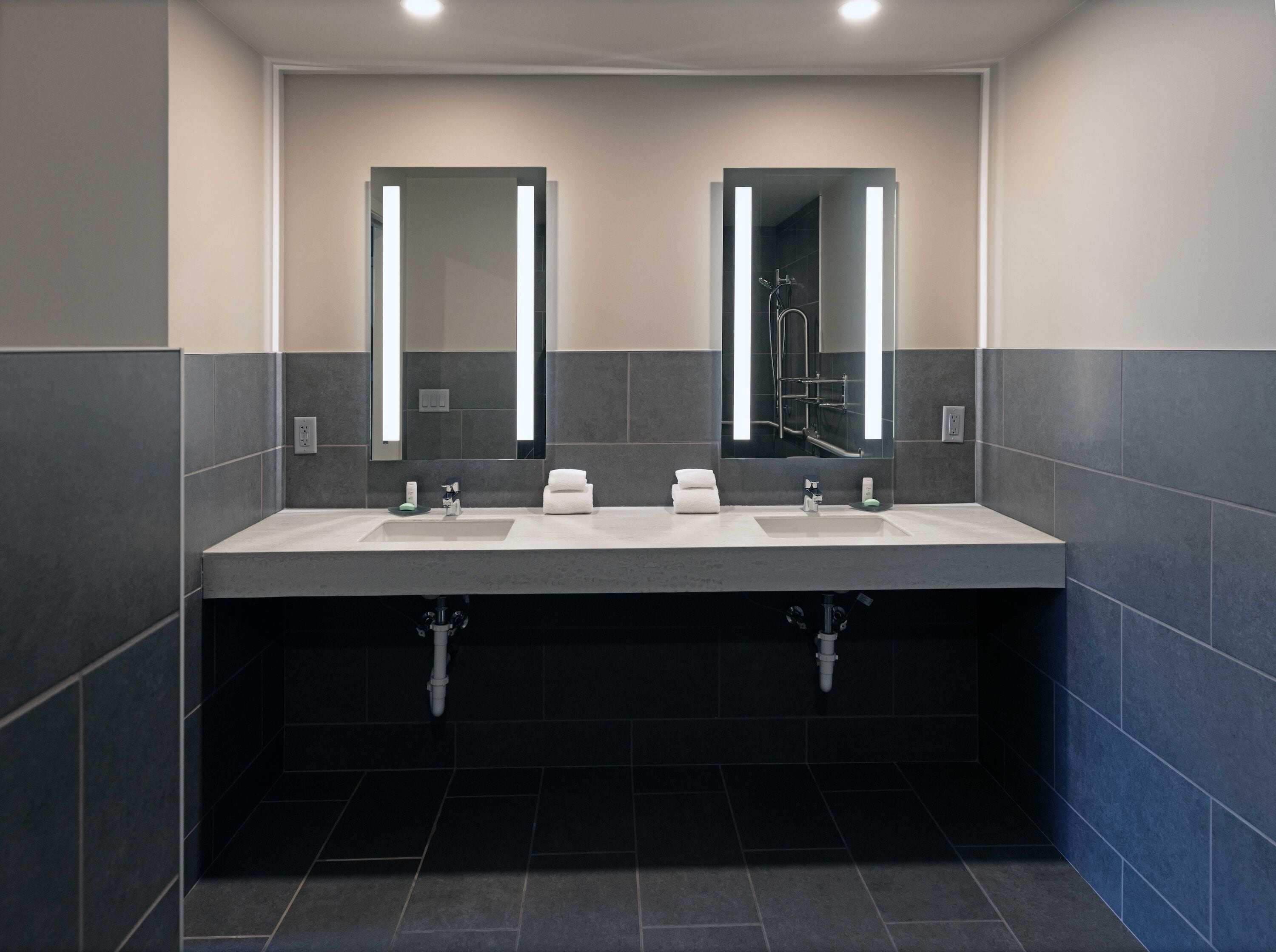 A modern bathroom with two sinks, large mirrors, and dark tiled walls.