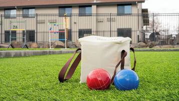 A bag on a grassy field with two sports balls, a building in the background.