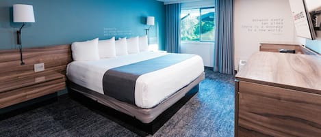 A modern hotel room with a large bed, a desk, and a view of the outdoors.
