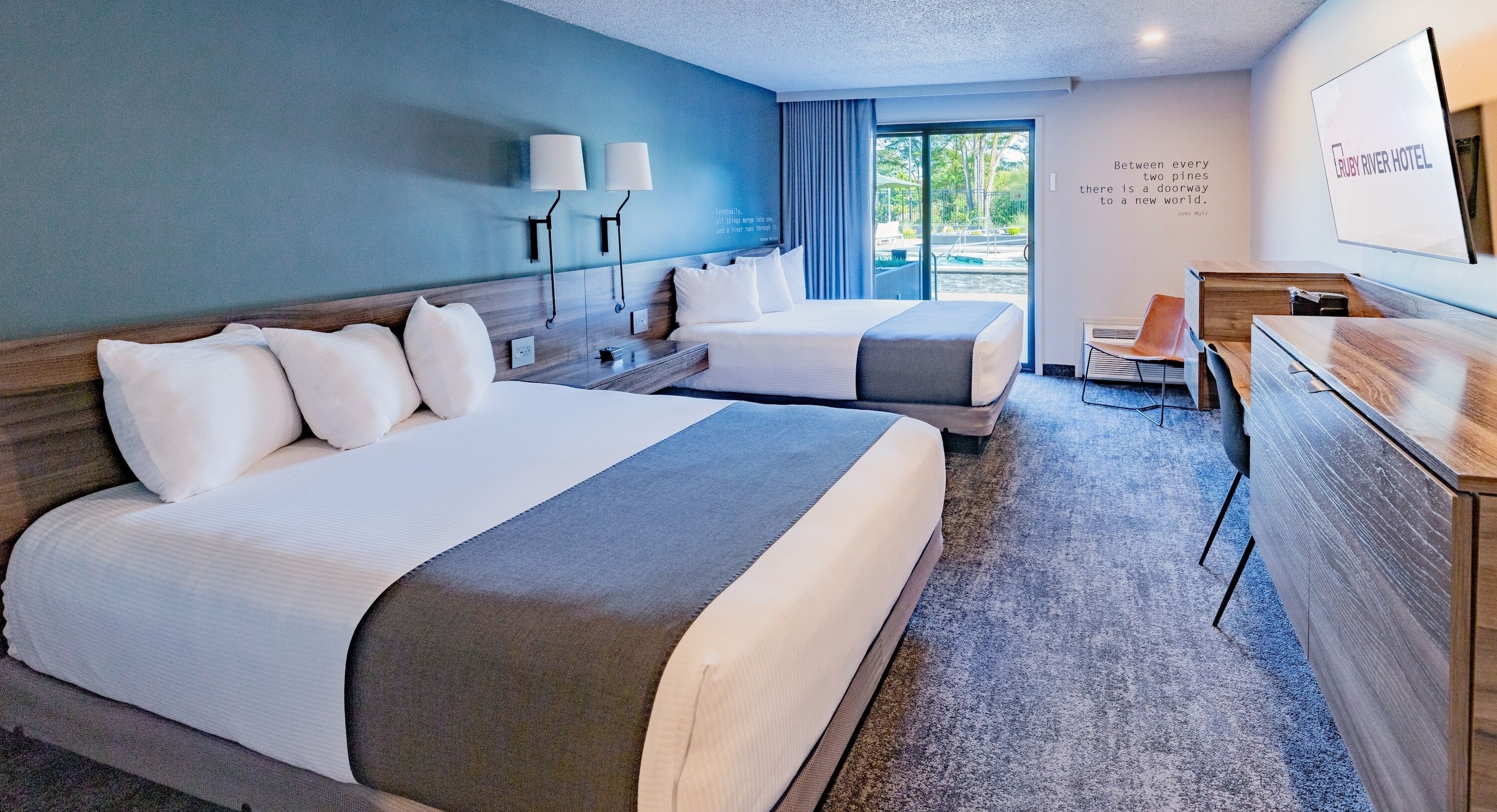 A hotel room with two beds, a desk, and a view of the outdoors.
