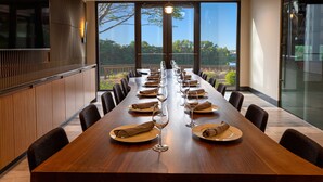 A long dining table set with plates, glasses, and napkins, with a view of trees and a balcony through large windows. - Ruby River Hotel Downtown Spokane (Spokane)