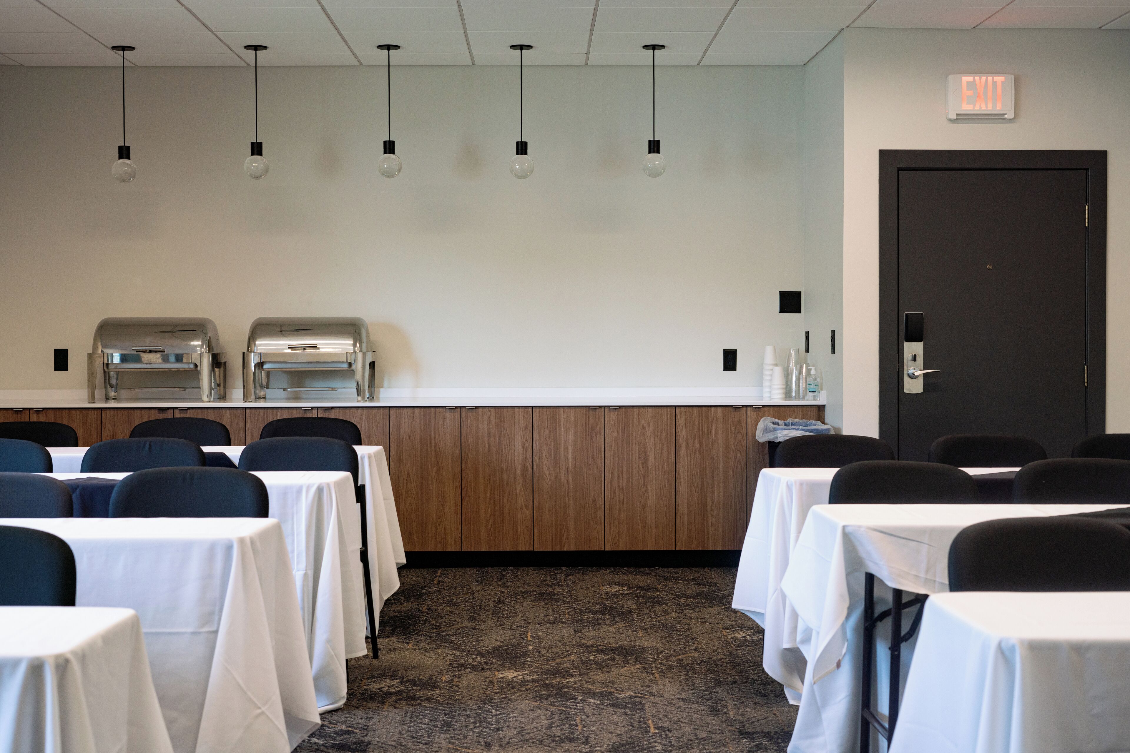 A conference room with tables, chairs, a kitchenette, and an exit door.