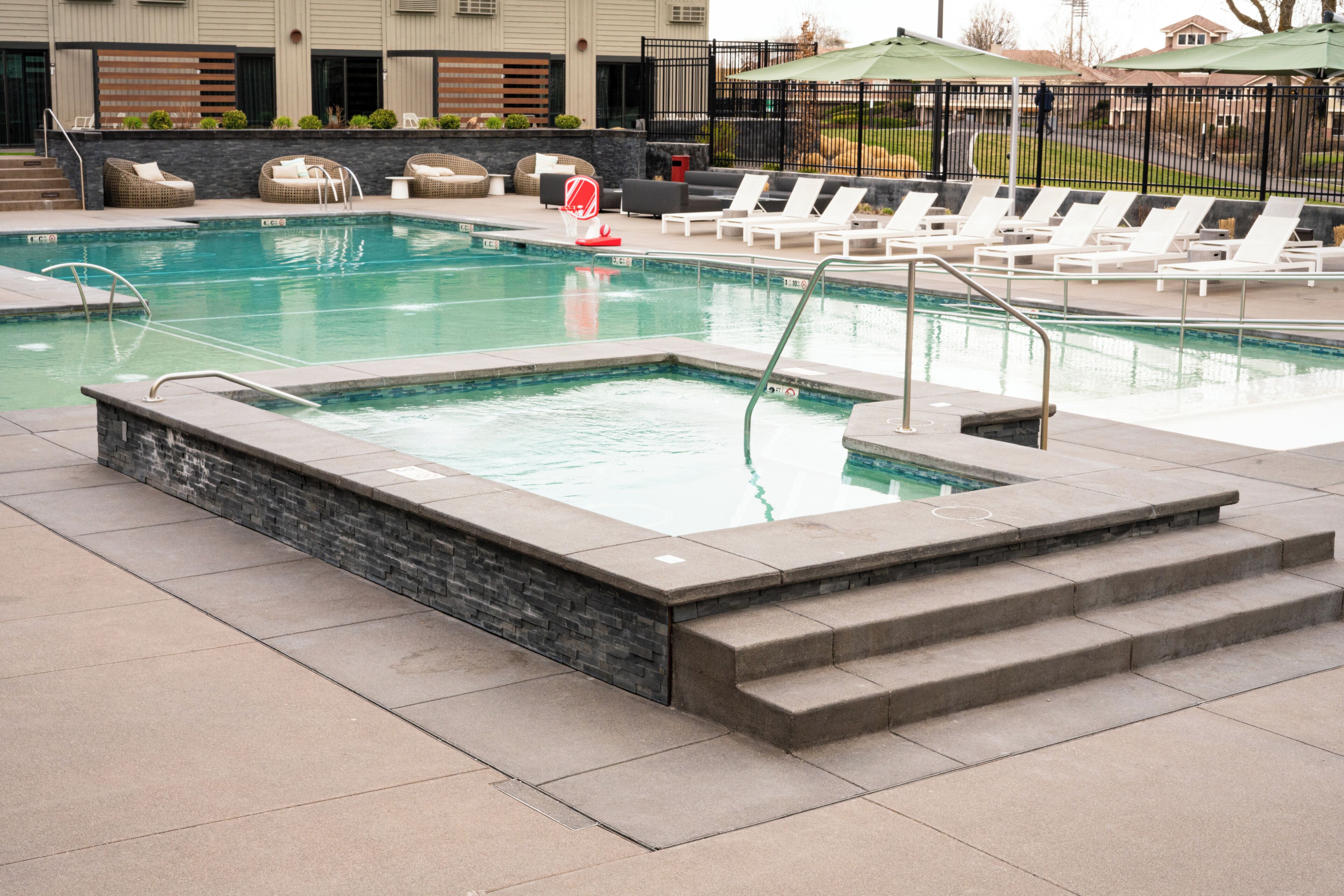 Une piscine rectangulaire avec des marches permettant d’y accéder, entourée de chaises longues et d’un mur en pierre.
