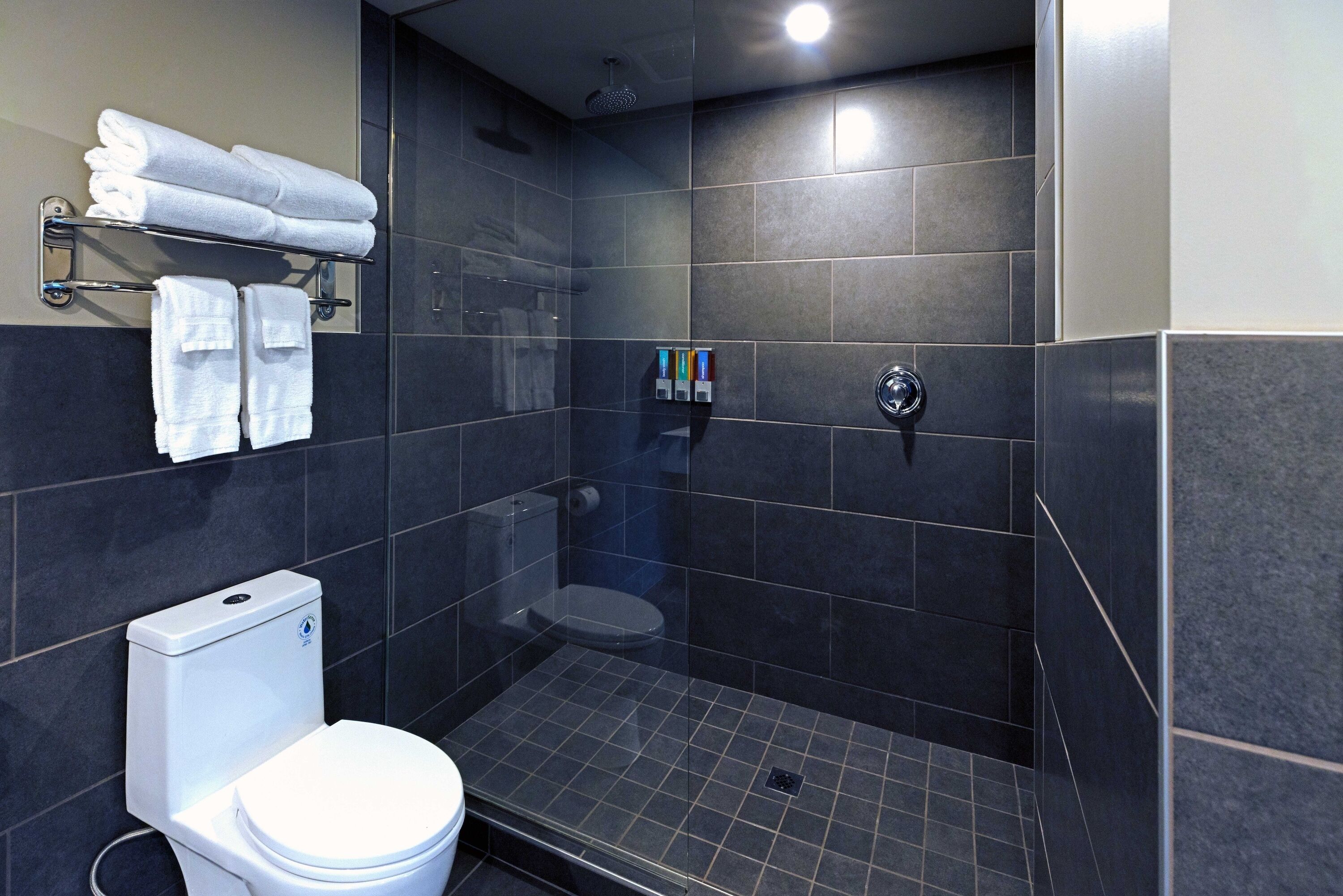 Een moderne badkamer met toilet, douchecabine en een handdoekrek met opgevouwen handdoeken.