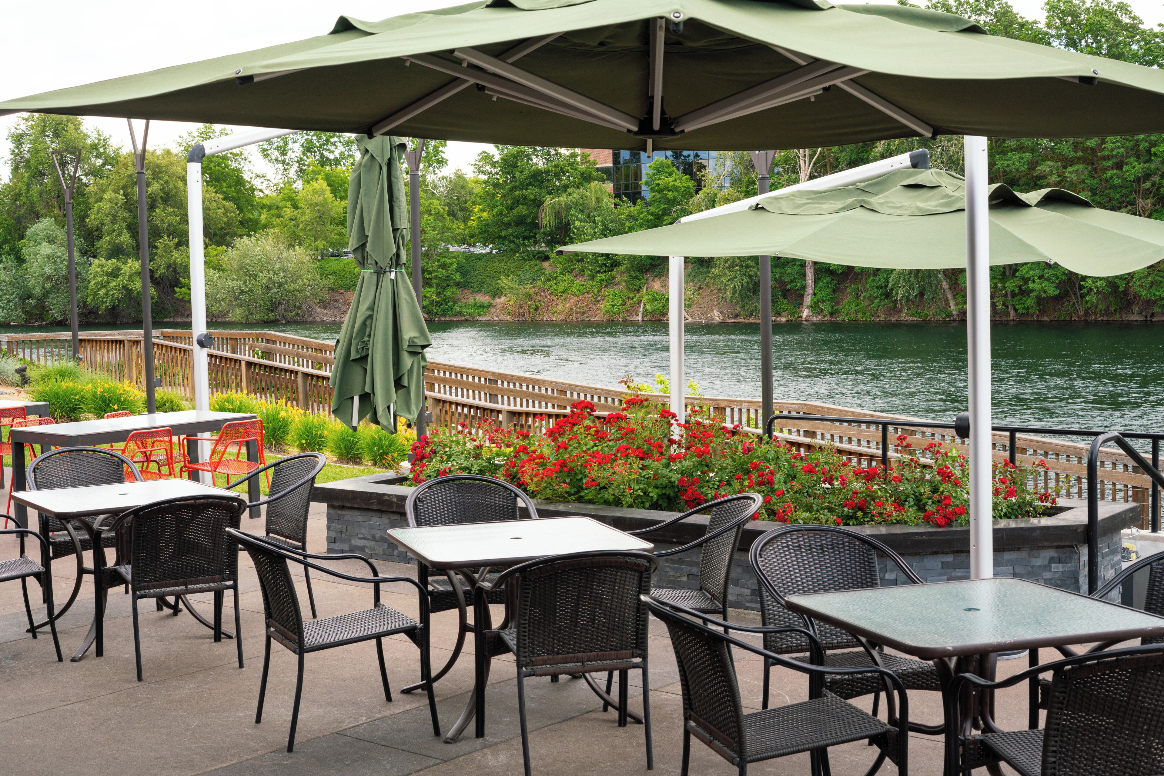 An outdoor patio with tables and chairs, a view of a river, and a wooden fence.