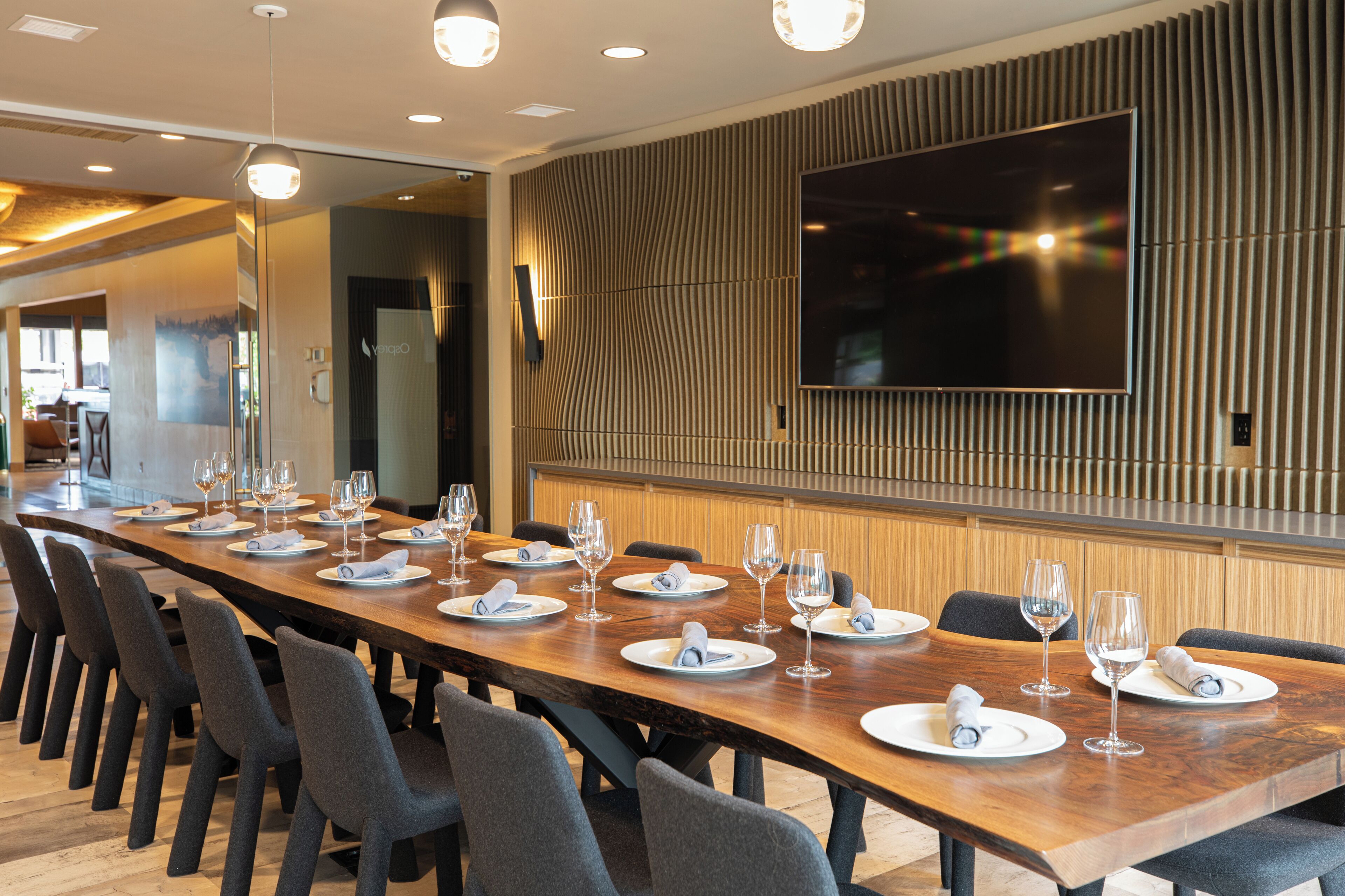A long dining table set for a meal with multiple chairs, a flat-screen TV mounted on the wall, and a modern interior design.