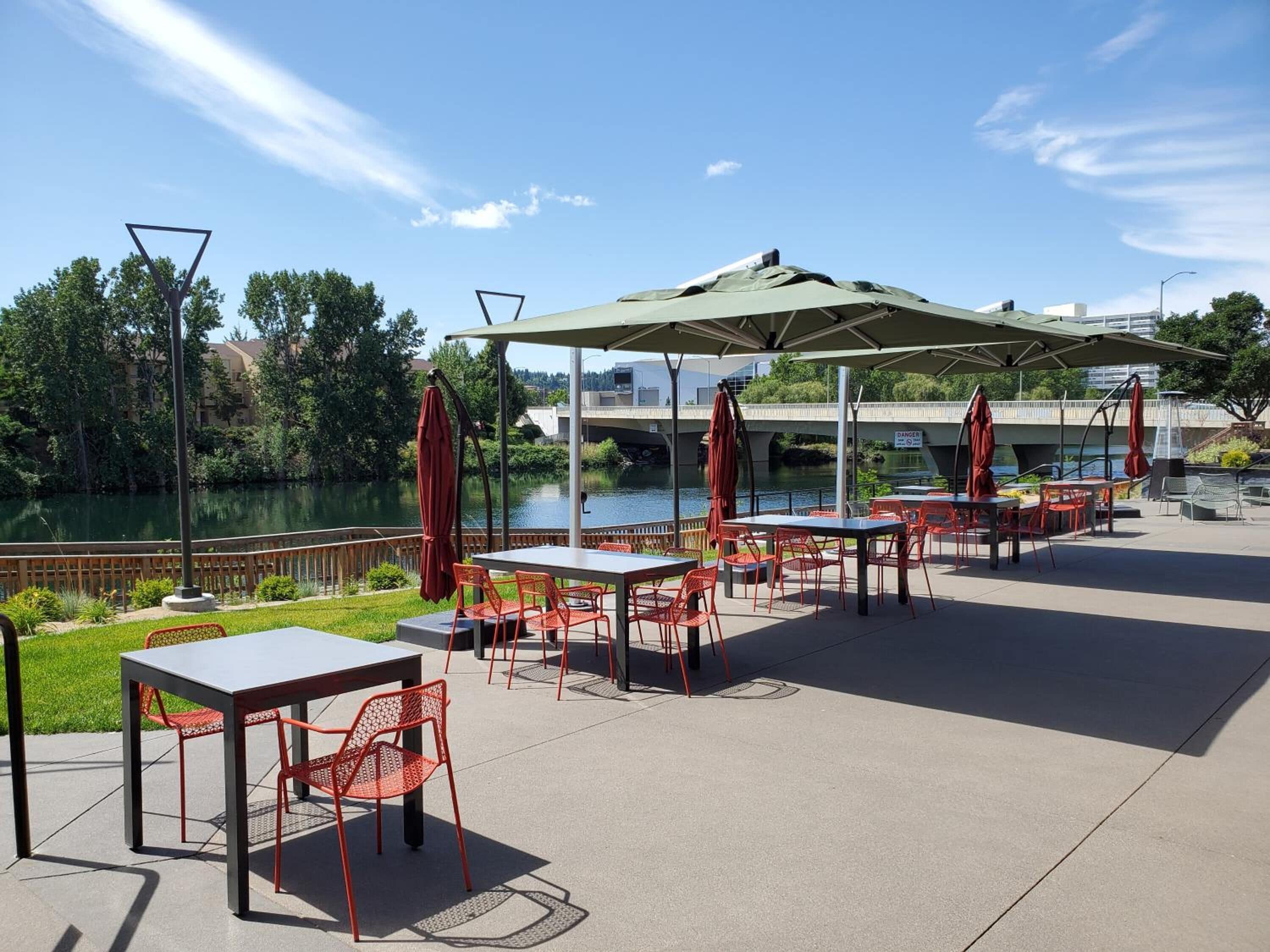 An outdoor patio with tables and chairs, a covered seating area, and a view of a body of water and a bridge.