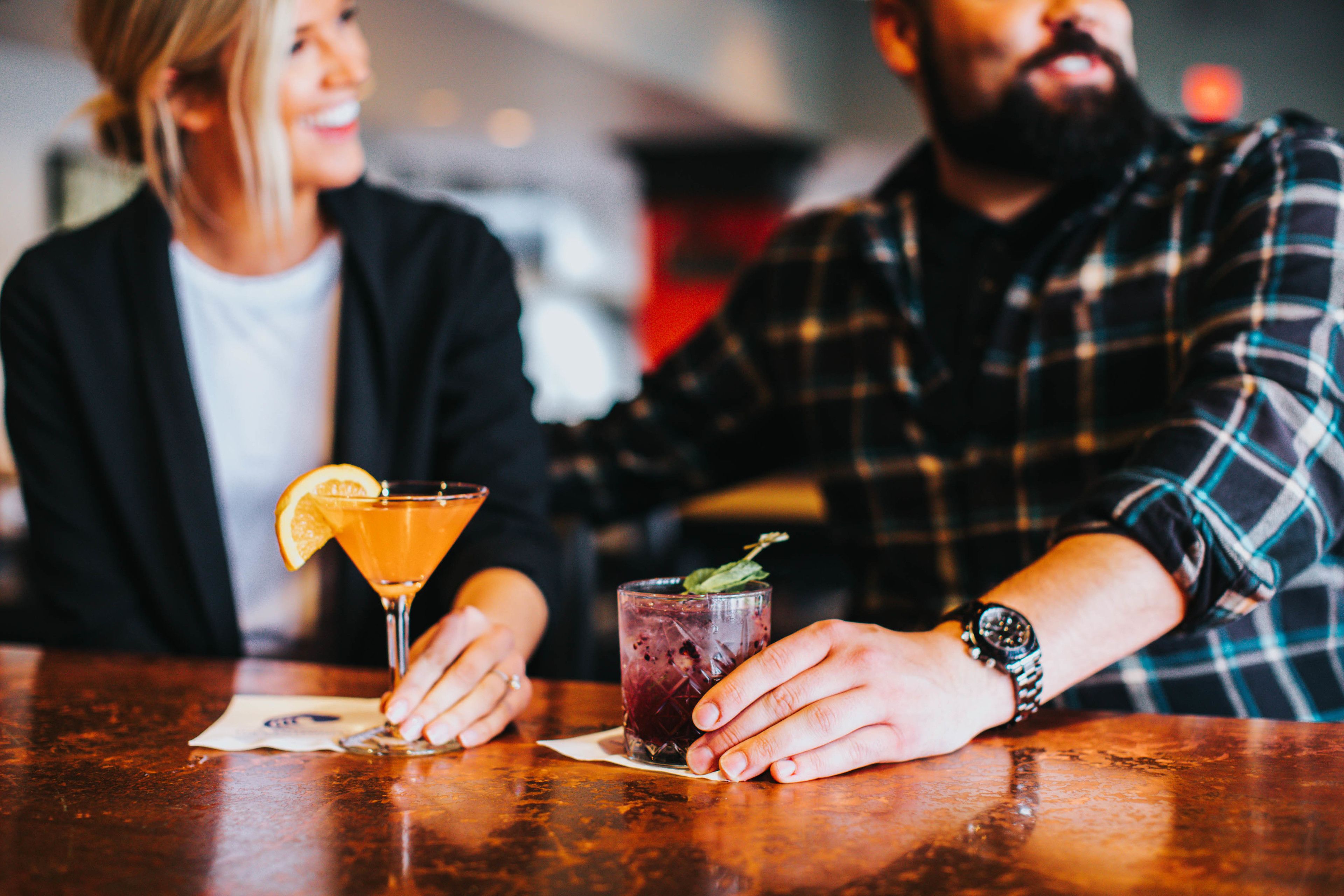 Two people sitting at a bar with drinks in front of them.