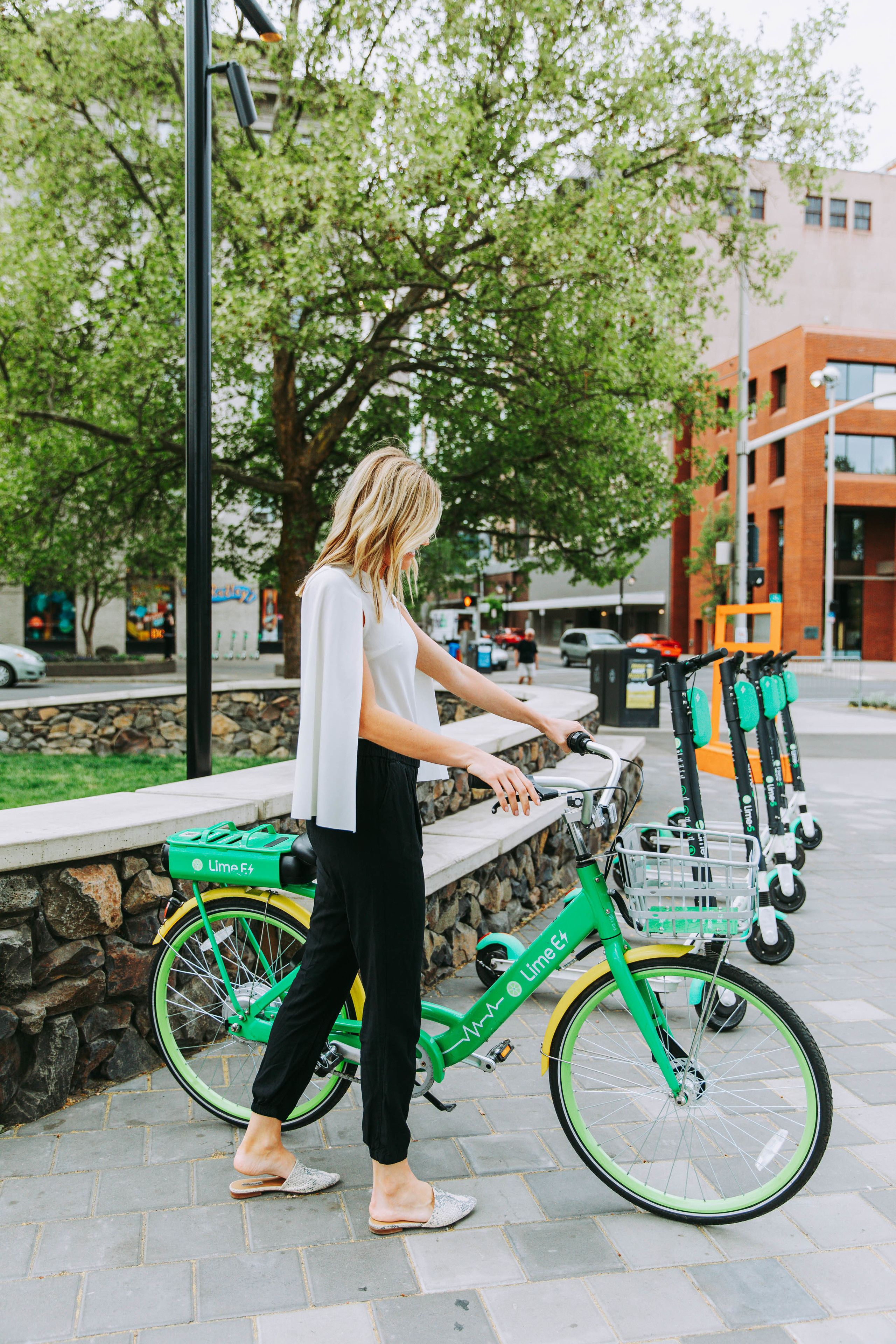 A person walking past a green bicycle with a basket, parked near a stone wall and a building.