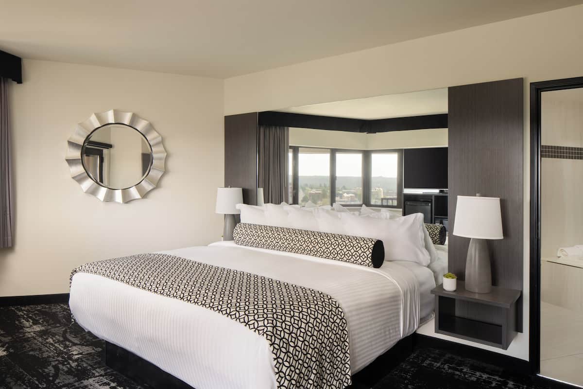 A hotel room with a large bed, two bedside tables, a mirror, and a view of the city.