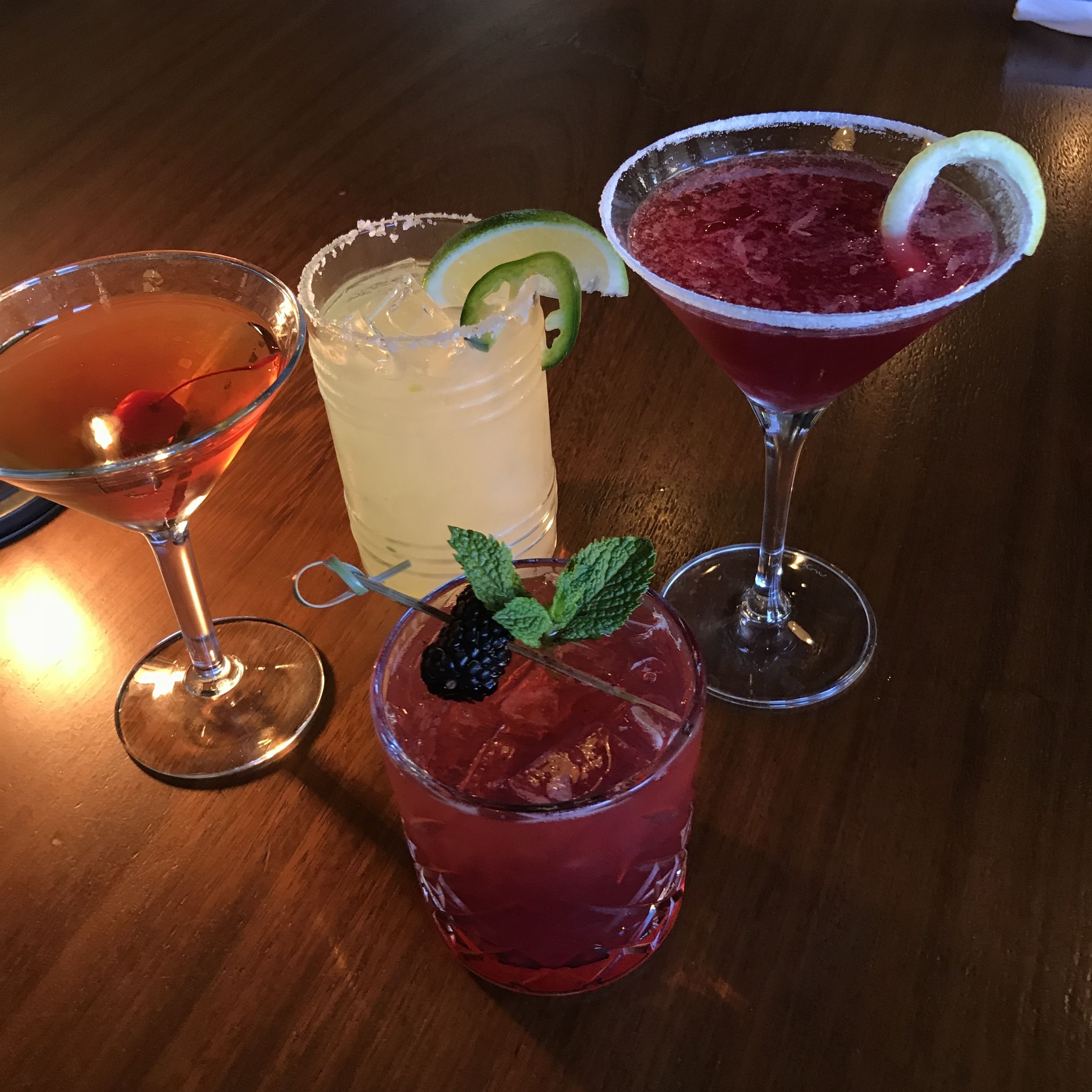 Vier verschiedene Cocktails auf einem Holztisch.