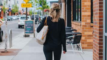 A woman walking on a sidewalk with a sign for 'Kendall Yards' and a pedestrian crossing sign.