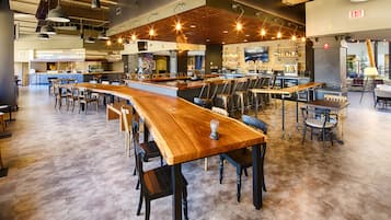 A spacious bar area with long wooden tables and chairs, a bar counter, and a seating area with sofas and tables.