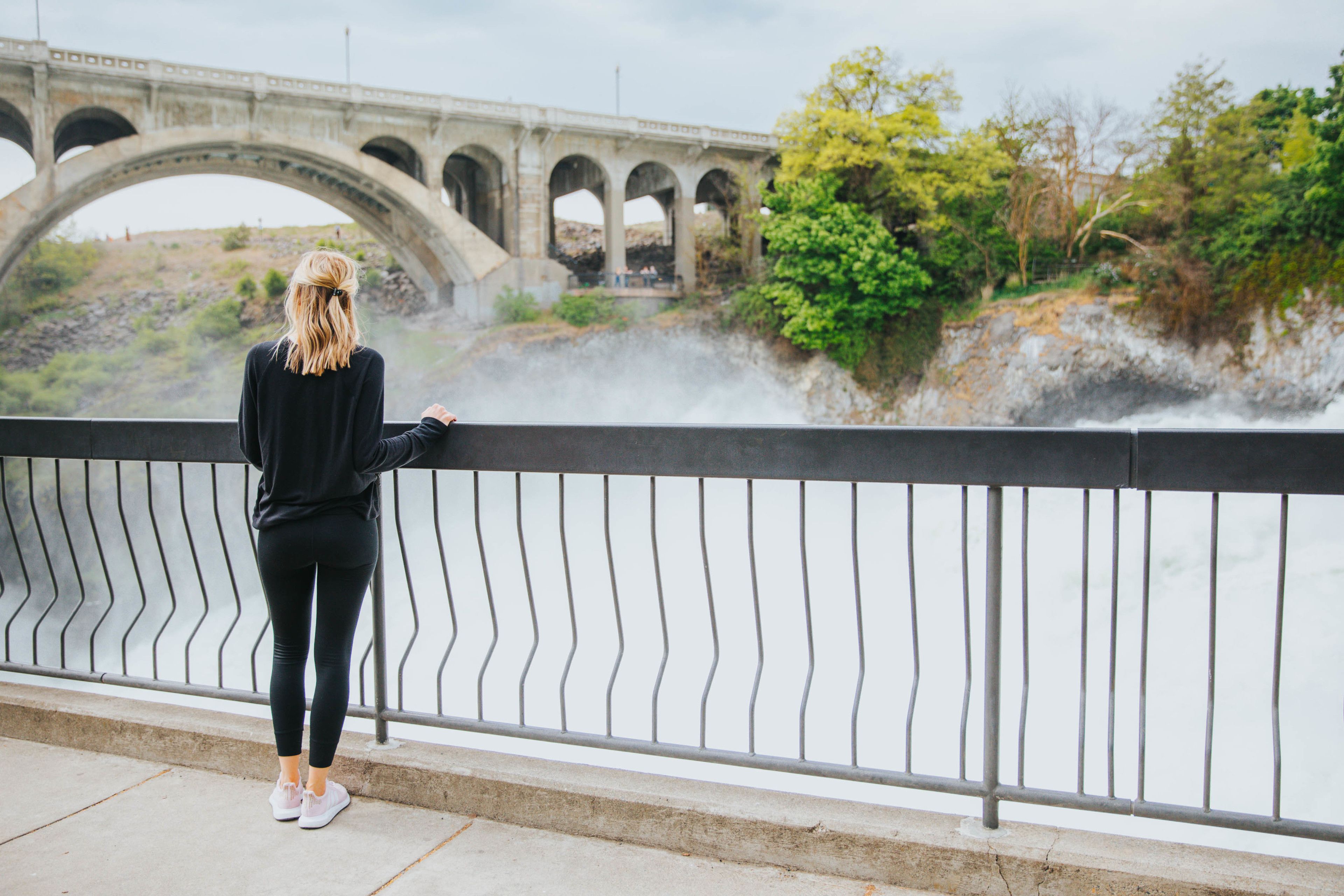 A person standing by a railing overlooking a bridge and a river.