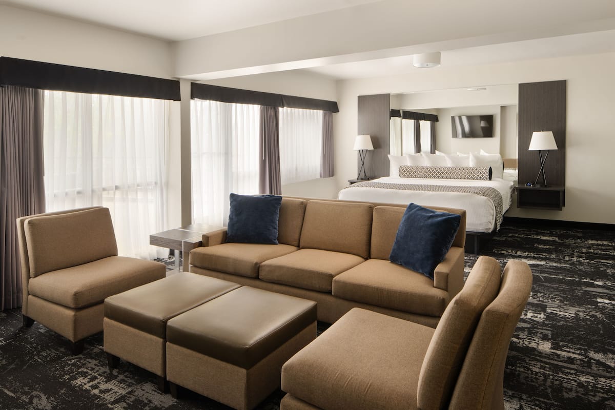 A hotel room with a large bed, a sofa, and a coffee table. There are two lamps on the side table and a TV on the wall.