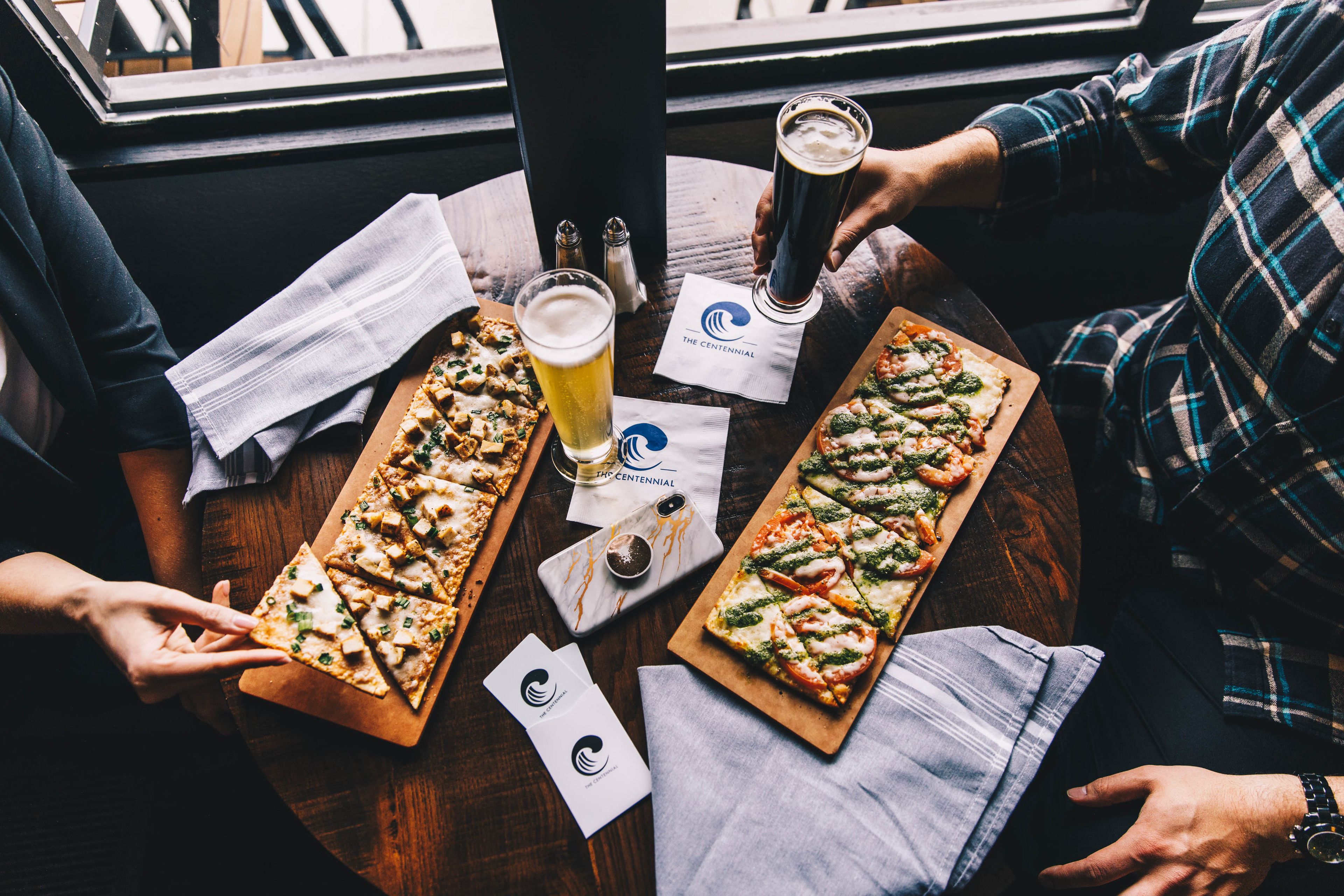 A wooden table with two pizzas, a glass of beer, and napkins.