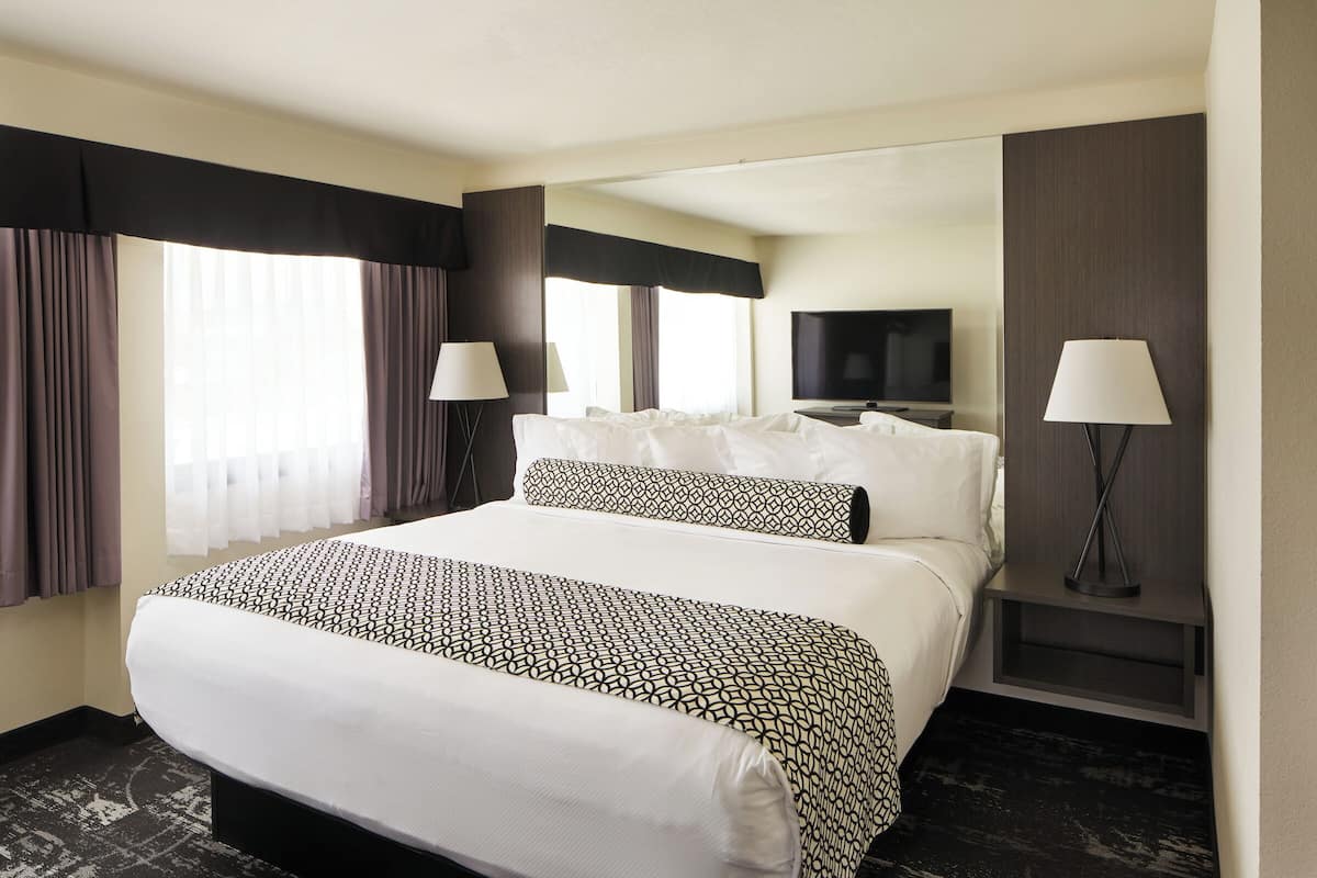 A hotel room with a large bed, two bedside tables, a TV, and a window with curtains.