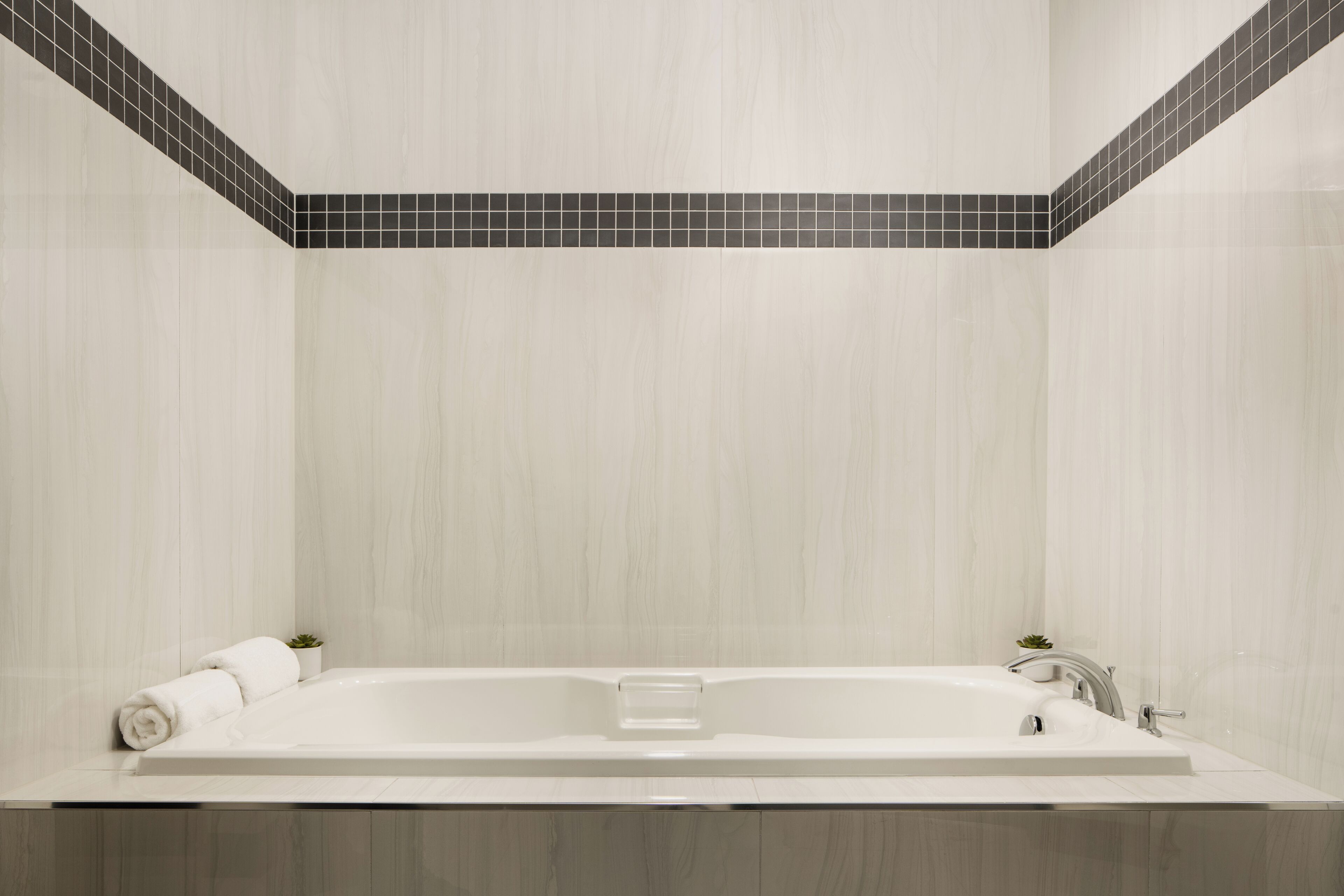 A modern bathroom with a large bathtub, a small potted plant, and a towel on the side.