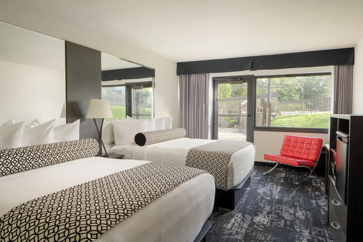 A hotel room with two beds, a red chair, a large window, and a view of the outdoors.